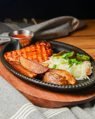 Sulu ızgara domuz bifteği, fırında patates, turşu ve domates sosu kırsal ahşap masa üzerinde servis edilir..