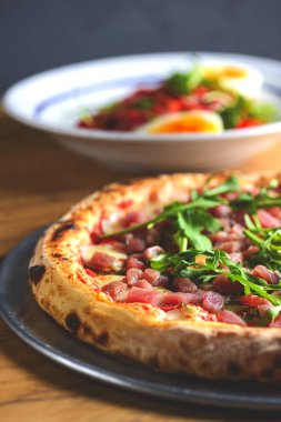 Sebzeli ton balığı salatası, haşlanmış yumurta, vişneli domates ve baharat. Somon balıklı pizza, peynir ve ahşap arka planda taze roka..