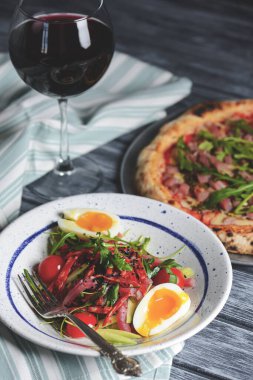 Sebzeli ton balığı salatası, haşlanmış yumurta, vişneli domates ve baharat. Somon balığı, peynir ve taze roka ile pizza ve ahşap zemin üzerinde bir bardak kırmızı şarap..
