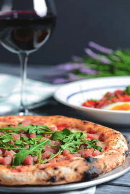 Sebzeli ton balığı salatası, haşlanmış yumurta, vişneli domates ve baharat. Somon balığı, peynir ve taze roka ile pizza ve ahşap zemin üzerinde bir bardak kırmızı şarap..