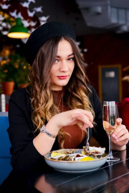 Restoranda bir tabak taze organik istiridye. Restoranda içki içen çekici genç bir kadın. Kafkasyalı kadın restoranda oturuyor, istiridye yiyor ve şampanya içiyor..