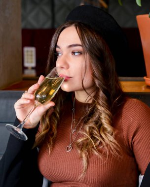 Restoranda içki içen çekici genç bir kadın. Kafkasyalı kadın restoranda oturuyor ve şampanya içiyor. Büyük bardakta şampanya. Konsepti tüketiyorum.