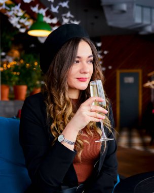 Restoranda içki içen çekici genç bir kadın. Kafkasyalı kadın restoranda oturuyor ve şampanya içiyor. Büyük bardakta şampanya. Konsepti tüketiyorum.