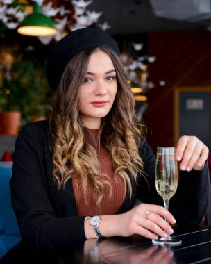 Restoranda içki içen çekici genç bir kadın. Kafkasyalı kadın restoranda oturuyor ve şampanya içiyor. Büyük bardakta şampanya. Konsepti tüketiyorum.