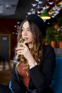 Restoranda içki içen çekici genç bir kadın. Kafkasyalı kadın restoranda oturuyor ve şampanya içiyor. Büyük bardakta şampanya. Konsepti tüketiyorum.