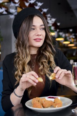 Soslu beyaz tabakta servis edilen kızarmış mozarella peyniri topları. Restoranda içki içen çekici genç bir kadın. Kafkasyalı kadın restoranda oturuyor, peynir yiyor ve şampanya içiyor..