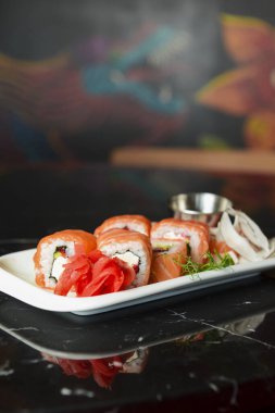 Kaliforniya ya da Philadelphia suşi dürümleri siyah arka planda beyaz tepside servis edilir. Japon mutfağı konsepti, geleneksel tarif.