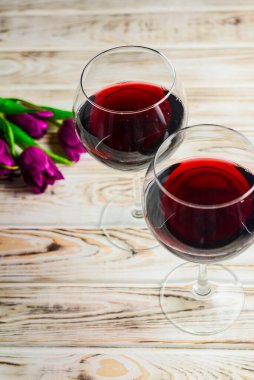 Ahşap zemin üzerinde iki kadeh kırmızı şarap ve laleler. Bahar çiçekleri, nasırlaşma, Uluslararası Kadınlar Günü.