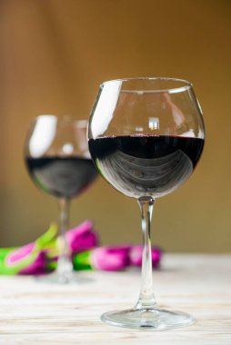 Ahşap zemin üzerinde iki kadeh kırmızı şarap ve laleler. Bahar çiçekleri, nasırlaşma, Uluslararası Kadınlar Günü.