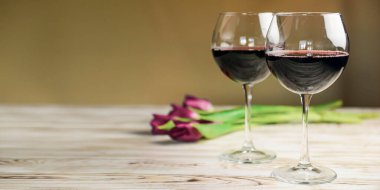 Ahşap zemin üzerinde iki kadeh kırmızı şarap ve laleler. Bahar çiçekleri, nasırlaşma, Uluslararası Kadınlar Günü.