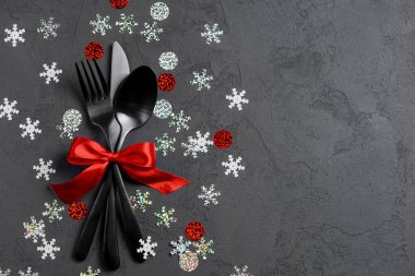 Çatal, bıçak, kaşık, çatal. Siyah arka plan. Üst manzara, düz yatış. Parlak kırmızı kurdeleli. Boşluk afişini kopyala.