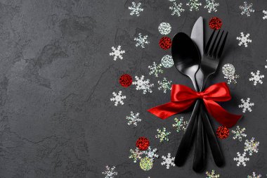 Çatal, bıçak, kaşık, çatal. Siyah arka plan. Üst manzara, düz yatış. Parlak kırmızı kurdeleli. Boşluk afişini kopyala.