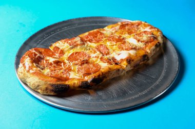 Mavi arka planda metal tepside servis edilen domuz pastırmalı, salamlı ve peynirli pizza. İtalyan mutfağı konsepti, geleneksel tarif.