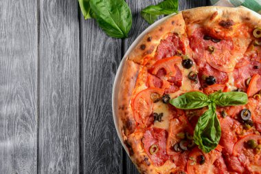 Salamlı taze İtalyan pizzası ve sade ahşap arka planda servis edilen siyah zeytinler. Geleneksel İtalyan pizza tarifi, İtalyan mutfağı. Uzay afişini kopyala. Fast food, abur cubur kavramı.