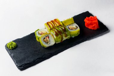 Beyaz arka planda yeşil ejderha suşisi yuvarlanıyor. Beyaz arka planda siyah bir tepside servis edilmiş. Geleneksel Japon mutfağı. Suşi Philadelphia ya da Kaliforniya.