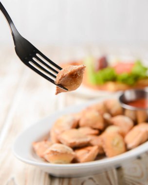 Etle doldurulmuş kızarmış hamur köftesi ve beyaz tabakta domates sosuyla servis edilmiş. Pelmeni tavada kızartılmış, Ukrayna mutfağı ve Rus mutfağı kavramı. Kırsal ahşap arka planda.