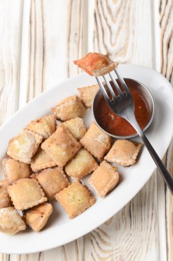 Etle doldurulmuş kızarmış hamur köftesi ve beyaz tabakta domates sosuyla servis edilmiş. Pelmeni tavada kızartılmış, Ukrayna mutfağı ve Rus mutfağı kavramı. Kırsal ahşap arka planda.