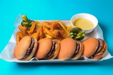 Dört hamburger, patates kızartması ve kızarmış tavuk mavi arka planda servis edilir. Abur cubur, arkadaşlarla parti konsepti..