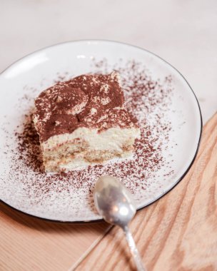 Geleneksel Tiramisu keki ahşap arka planda beyaz bir tabakta servis edilir. İtalyan mutfağı konsepti, lezzetli çikolatalı tatlı..