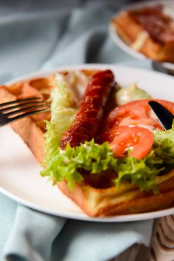 Waffle sağlıklı kahvaltı. Izgara sosisli ekşi waffle, lezzetli sos ve taze sebzeler. Waffle üzerinde marul salatası olan sebzeler. Hafif ahşap arkaplanda servis edilir