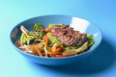 Kızarmış sığır eti, avokado dilimleri, turp, lahanalar, brokoli ve zencefil şeritli taze yaz salatası mavi arka planda servis edilir. sağlıklı yeme kavramı.