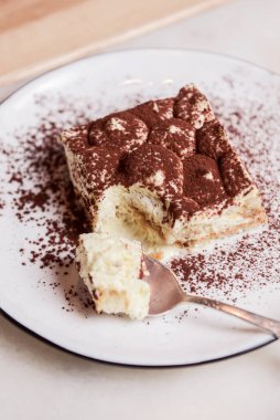 Geleneksel Tiramisu keki ahşap arka planda beyaz bir tabakta servis edilir. İtalyan mutfağı konsepti, lezzetli çikolatalı tatlı..