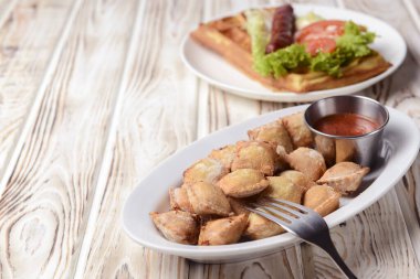 Etle doldurulmuş kızarmış hamur köftesi ve beyaz tabakta domates sosuyla servis edilmiş. Pelmeni tavada kızartılmış, Ukrayna mutfağı ve Rus mutfağı kavramı. Kırsal ahşap arka planda.