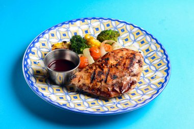 Lezzetli ızgara biftek, bol sebzeli ve mısır, beyaz bir tabakta servis ediliyor ve mavi arka planda sos var. BBQ konsepti.