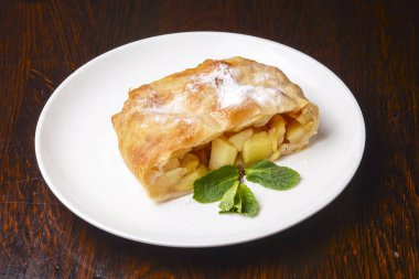 Ahşap masa zemininde beyaz bir tabakta servis edilen lezzetli fırınlanmış Rustik elmalı turta dilimi. Lezzetli sağlıklı tatlı..