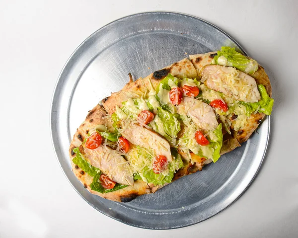 Pinza with chicken, cherry tomatoes, lettuce salad and Worcestershire sauce cooked in an oven with wood and served on a metal tray over white background. Traditional recipe, pizza or pinza.
