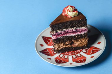 Mavi arka planda renkli bir tabakta çikolatalı vişneli pasta. Pastanın tamamından bir dilim pasta. Tatlı zamanı..