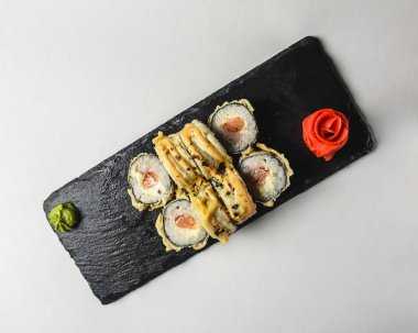 Japon suşi rulosu - Somon ve krem peynirli sıcak suşi rulosu beyaz arka planda siyah tahtada servis ediliyor. Japon mutfağı kavramı.