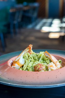 Ev yapımı pesto soslu karidesli spagetti. Restoranda servis edilen karidesli ıspanaklı makarna. Arka plan bulanık. İtalyan mutfağı kavramı.