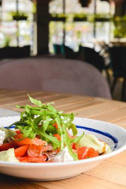 Peynirli ve baharatlı domates ve somon salatası. Geleneksel İtalyan mutfağı, İtalyan konsepti. Restorandaki ahşap bir masada beyaz bir tabakta servis edilmiş. Konsepti tüketiyorum.