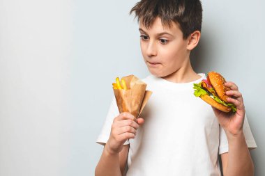 Elinde abur cubur olan küçük mutlu çocuk: patates kızartması ve hamburger. Fast food. Sağlıksız gıda kavramı. Beyaz arka planda. Boşluk afişini kopyala.