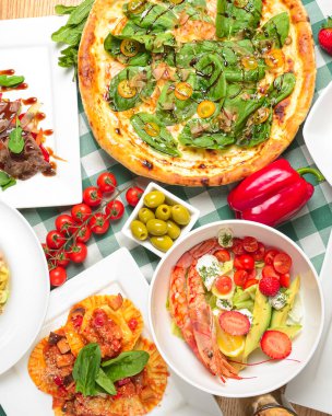 Ton balığı ve ıspanaklı pizza, karidesli salata ve avokado, raviolli, deniz makarnası, çikolatalı kremalı vanilyalı peynirli kek ve taze çilek. İtalyan mutfağı konsepti, İtalyan yemekleri..