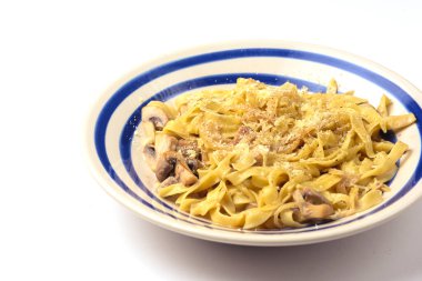 Beyaz arka planda servis edilen parmesan peynirinin altında tavuk ve mantarlı makarna. İtalyan mutfağı konsepti, lezzetli yemek..