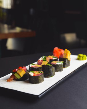 Maki suşisi siyah arka planda beyaz bir tabak üzerine kurulmuş. Japon mutfağı konsepti, zencefil ve wasabi soslu maki dürümleri..