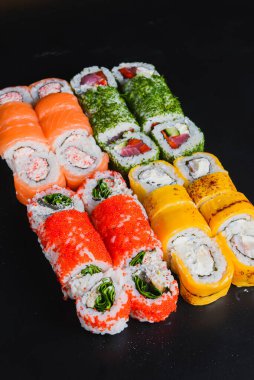 Suşi seti nigiri ve suşi ruloları siyah taş arka planda servis edilir. Japon mutfağı konsepti, ton balığı ve somon rulosu, Philadelphia ve Kaliforniya çedar peynirli suşi.