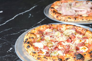 Taze İtalyan pizzası. Siyah taş masada servis edilmiş. Geleneksel tarif, İtalyan mutfağı konsepti. Pastırmalı pizza ve jambonlu pizza restoranda ya da pizzacıda servis edilir..