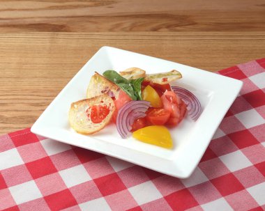 Soğanlı taze domates salatası ve kırmızı ekose masa örtüsüyle birlikte ahşap bir tabakta servis edilen kızarmış ekmek. Sağlıklı öğle ve akşam yemeği konsepti.