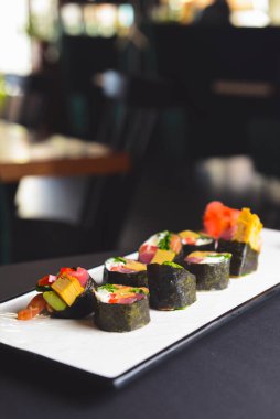 Maki suşisi siyah arka planda beyaz bir tabak üzerine kurulmuş. Japon mutfağı konsepti, zencefil ve wasabi soslu maki dürümleri..