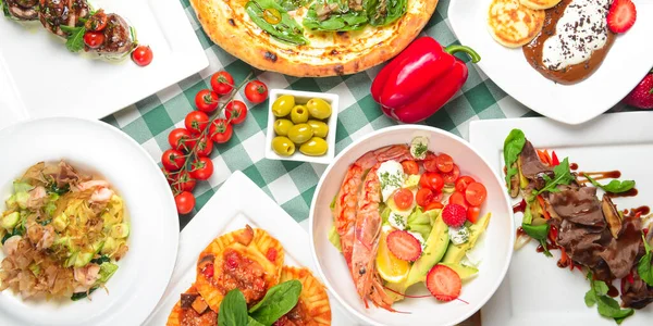 Tuna and spinach pizza, salad with shrimps and avocado, raviolli, sea foos pasta, vanilla cheesecakes with chocolate cream and fresh strawberries. Italian cuisine concept top view Italian dishes.