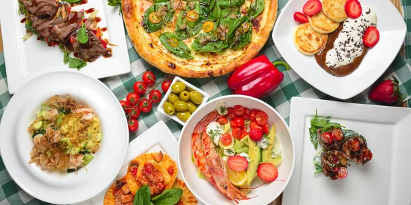 Tuna and spinach pizza, salad with shrimps and avocado, raviolli, sea foos pasta, vanilla cheesecakes with chocolate cream and fresh strawberries. Italian cuisine concept top view Italian dishes.