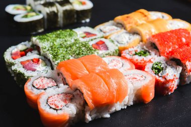 Suşi seti nigiri ve suşi ruloları siyah taş arka planda servis edilir. Japon mutfağı konsepti, ton balığı ve somon rulosu, Philadelphia ve Kaliforniya çedar peynirli suşi.