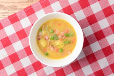 Geleneksel taze bezelye çorbası beyaz kâsede kırmızı ekose masa örtüsünün üzerinde. Sağlıklı yemek, taze çorba..