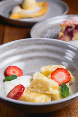 Ekşi kremalı vanilyalı tatlı ve taze organik çilekli. Geleneksel bir kase içinde koyu renkli ahşap masada servis edilmiş. Gürcü mutfağı konsepti. Lezzetli vanilyalı meyve tatlısı.