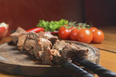 Salamura edilmiş şiş kömürün üstünde ızgarada pişirilmiş. Shashlik ya da Shish kebap, arka planda domatesler olan tahta bir tahtada servis edilir. Mangalda Biftek Kebabı..