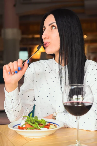 Genç ve çekici bir kadın restoranda sağlıklı bir öğle yemeği yiyor. Siyah saçlı beyaz bir kadın yemek yiyor. Covid-19 salgını yüzünden restoranda tek başına yemek yemek..