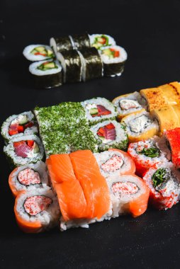 Suşi seti nigiri ve suşi ruloları siyah taş arka planda servis edilir. Japon mutfağı konsepti, ton balığı ve somon rulosu, Philadelphia ve Kaliforniya çedar peynirli suşi.